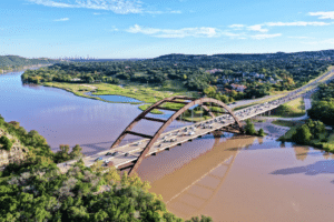 Cars drive over the Pennybacker Bridge during rush hour with a view of the Austin skyline.